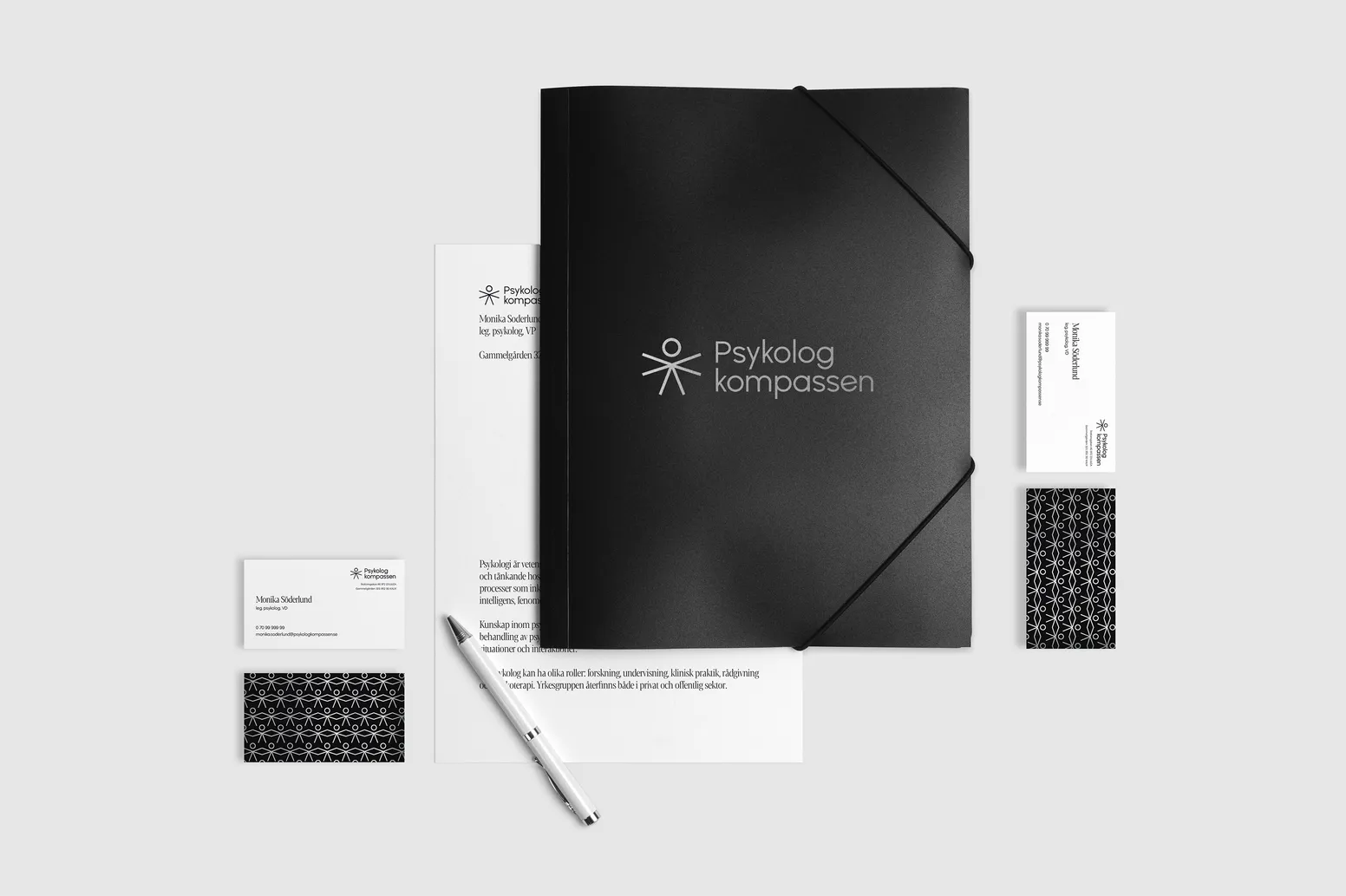 a stationery set presenting Psykologkompassen branding, including two sides of the business card, a black folder with the logo, a piece of branded paper and a white pen