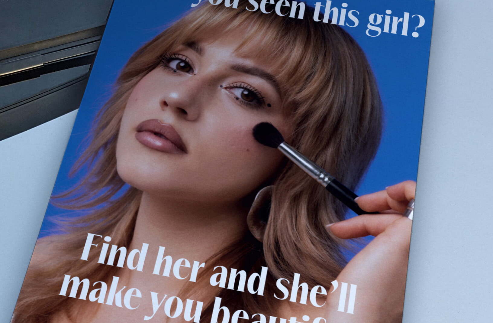 Makeup artist’s poster on a car hood, featuring a woman with glam makeup and text promoting her services with a website link.