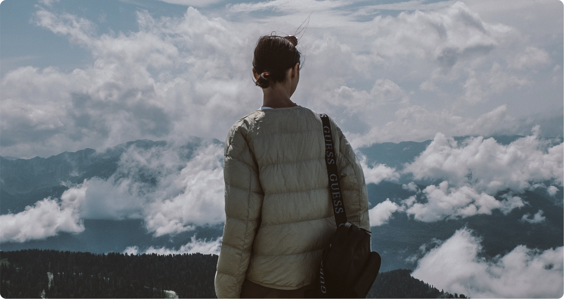 a woman facing away from the camera looks at the landscape view in front of her - on this background a logo of Psykologkompassen brand is displayed