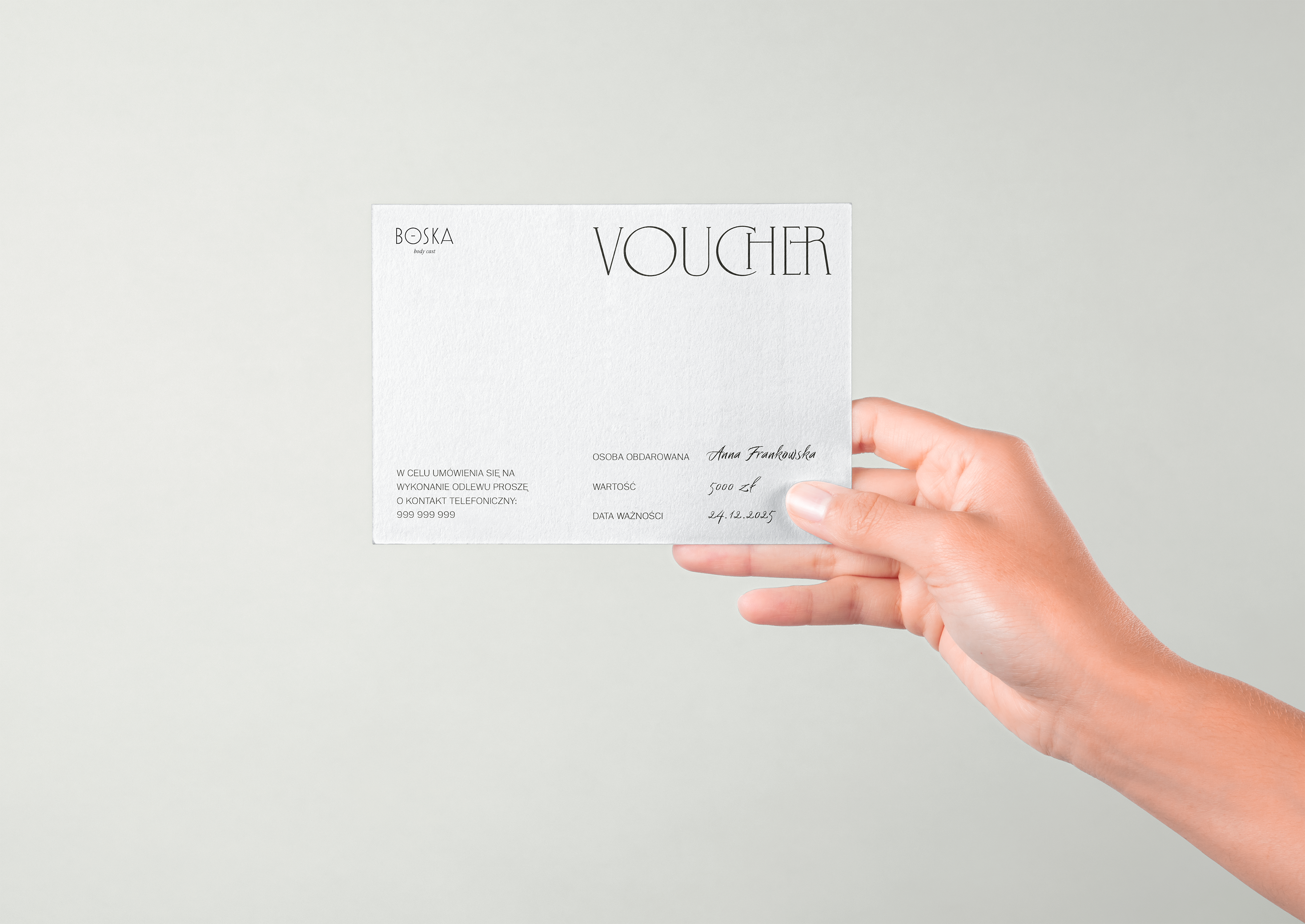 a hand holding a voucher in minimalistic design printed on a white textured paper