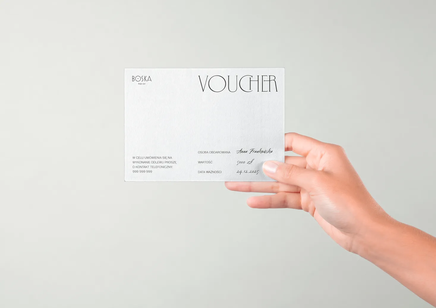 a hand holding a voucher in minimalistic design printed on a white textured paper